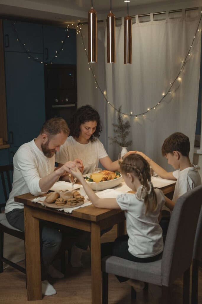 pexels-photo-5813816 A family holding hands and praying around a festive dinner table set with food and decorations.